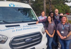 Six people stand near the front of a white van. They're all employee's of Joseph's House.