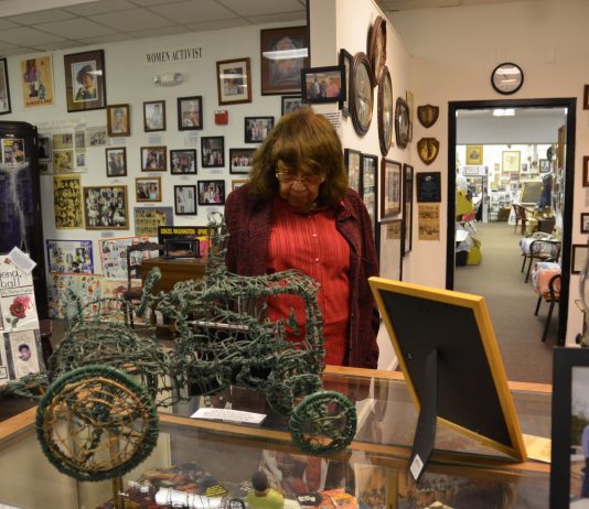 A woman wearing a redish sweater and shirt look at at a piece of history at the Jack Hadley Black History Museum in Thomasville, Georgia. She is surrounding by other artifacts.
