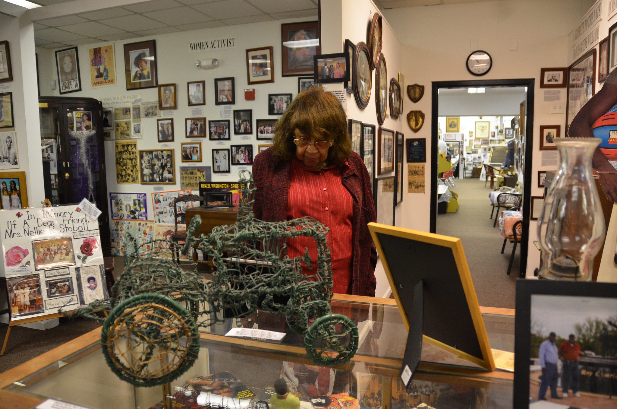 A woman wearing a redish sweater and shirt look at at a piece of history at the Jack Hadley Black History Museum in Thomasville, Georgia. She is surrounding by other artifacts.