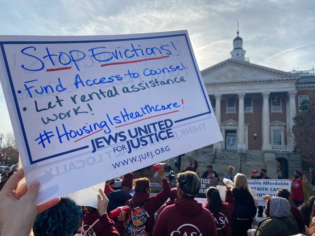 A closeup of a handwritten sign held aloft at a rally at the Maryland State House. The handwritten part says: Stop Evictions! Fund Access to Counsel. Let rental assistance work! #HousingIsHealthcare. The printed part of the sign indicates that it's by Jews United for Justice.