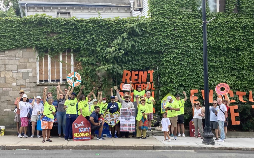 A group of about 30 people, many wearing CLVU's bright yellow-green T-shirts, hold posters and banners advocating for rent control. Photo by Grace Holley, CLVU