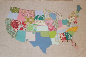 A patchwork map of the continental U.S., with a different fabric for each state. Some fabrics are solids, some prints, tending toward stylized florals. The state lines have been embroidered with contrasting thread colors.