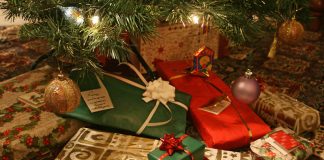 A pile of presents wrapped in red and green paper with bows, beneath a Christmas tree.
