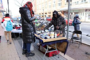 Two people in dark winter coats stand at a table alongside a city street.