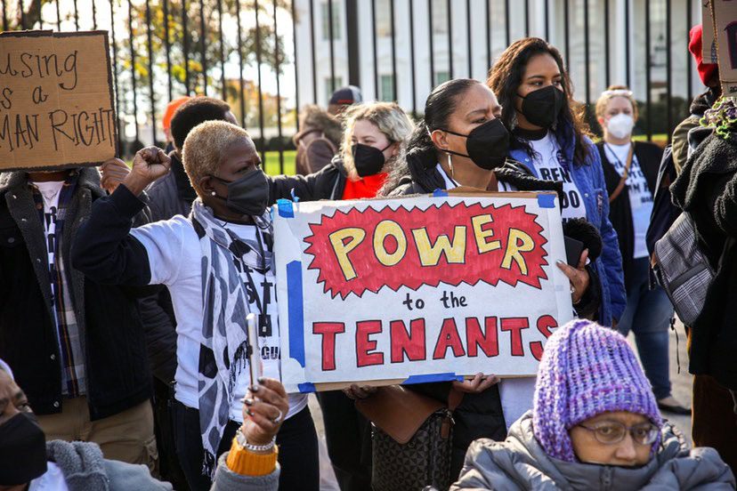 Two women in a crowd of protesters hold a big hand-lettered sign that says "Power to the tenants." Other people near and behind them are also holding signs supporting renters rights.