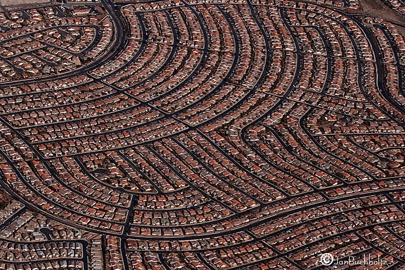 Aerial view of a suburb with hundreds of houses built close together on curving streets and no sign of green anywhere