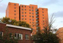 An orangey multistory apartment building with a smaller brick building in the foreground.