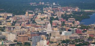 An aerial view of Madison, Wisconsin, with a lake in the foreground, the capital dome visible beyond it, and the city stretching beyond that.