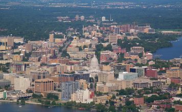 An aerial view of Madison, Wisconsin, with a lake in the foreground, the capital dome visible beyond it, and the city stretching beyond that.