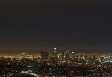 A nighttime view of Los Angeles from a distance, with glittering lights and above them a sky that's not altogether dark.