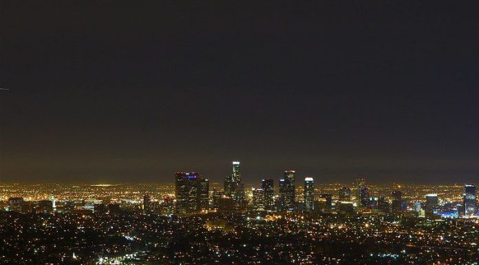 A nighttime view of Los Angeles from a distance, with glittering lights and above them a sky that's not altogether dark.