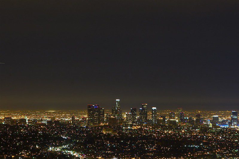 A nighttime view of Los Angeles from a distance, with glittering lights and above them a sky that's not altogether dark.