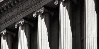 A tightly cropped black-and-white view of stone Ionic columns at the entrance to a courthouse. Words are carved on the lintel over the columns; visible in this photo are "and blessing."
