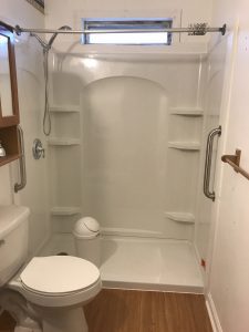 After modifications, an accessible shower: It has a very low threshold to step in, built-in shelves at various heights for toiletries, and at right, a long vertical grab bar for people of different heights.
