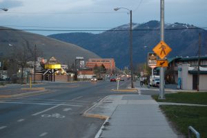 A roadway in Missoula, Montana. There are some buildings to the right, and mountains in the back.