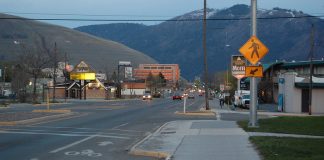 A roadway in Missoula, Montana. There are some buildings to the right, and mountains in the back.