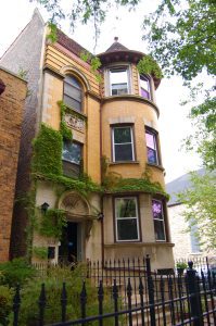 A three-story yellow building with moss growing in the first floor entrances and second floor.