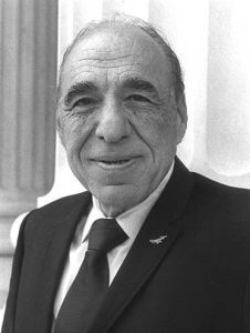 Black and white headshot of Henry Gonzalez, a smiling middle-aged man in a suit.