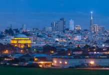 A night view of San Francisco, with a dark blue sky and golden lights shining in all the windows.