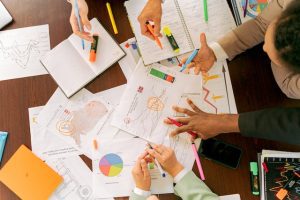 View from above of the hands of several co-workers discussing maps and charts. (representing the idea of technical assistance)