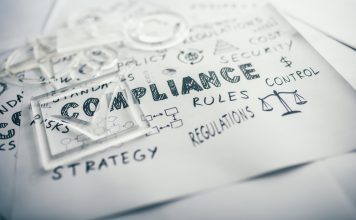 Transparent check mark over compliance related icons and words handwritten on white papers