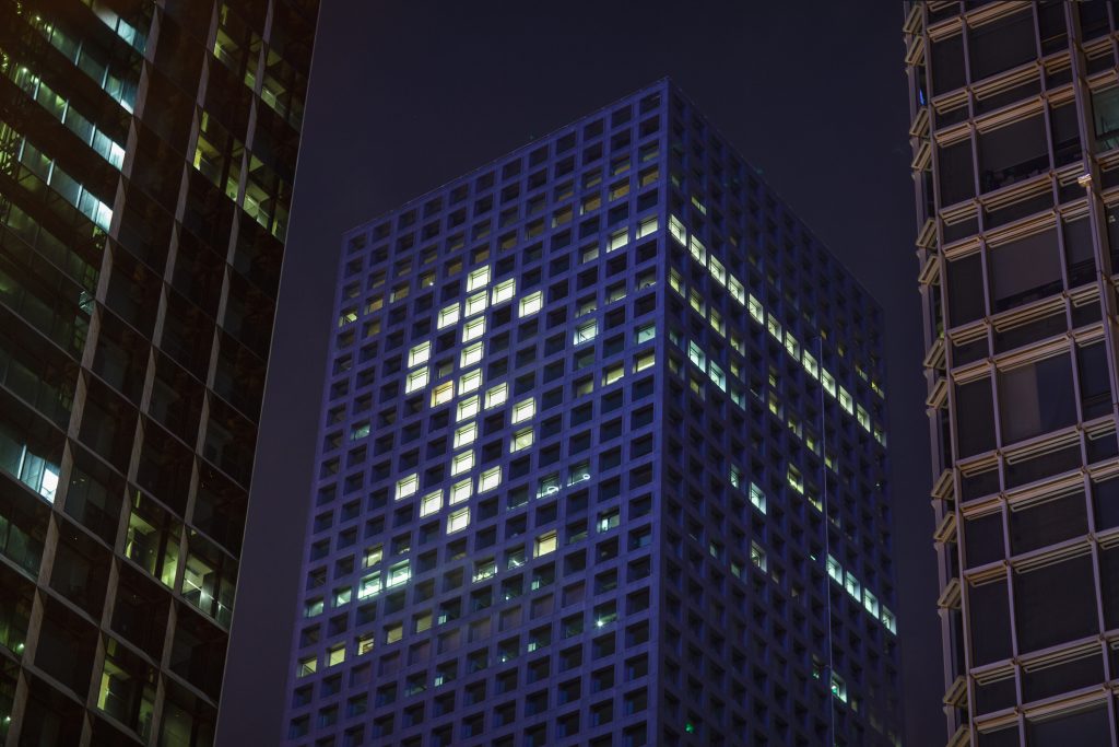 A skyscraper at night with windows lit up to form a large dollar sign.