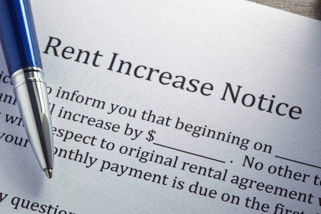 Close-up of document titled "Rent Increase Notice." Text is partly hidden by a blue and silver ballpoint pen. Visible text says "...inform you that beginning on ____ .... increase by $_____. No other ..... to original rental agreement.... monthly payment is due on the first...."
