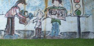 A large graffiti'd mural, painted in a cartoonish style, showing an apparently homeless family of three standing near a traffic light. The mother is handing a box or carton of stuff to the child, whose other hand is reaching to the father figure. He is holding up a sign that says "Help us." Facial features were not drawn on these figures, giving them a universal quality.