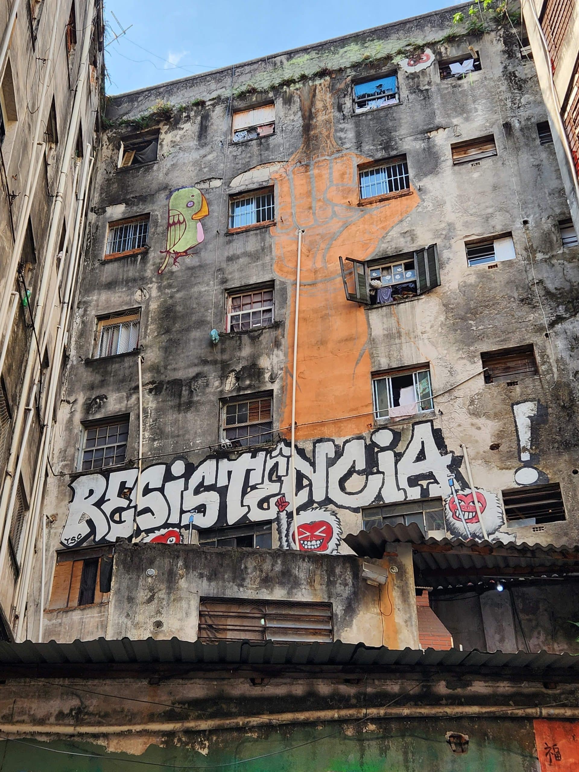 The exterior of a building, with lettering that reads "Resistencia" with a mural of a fist extending upward.