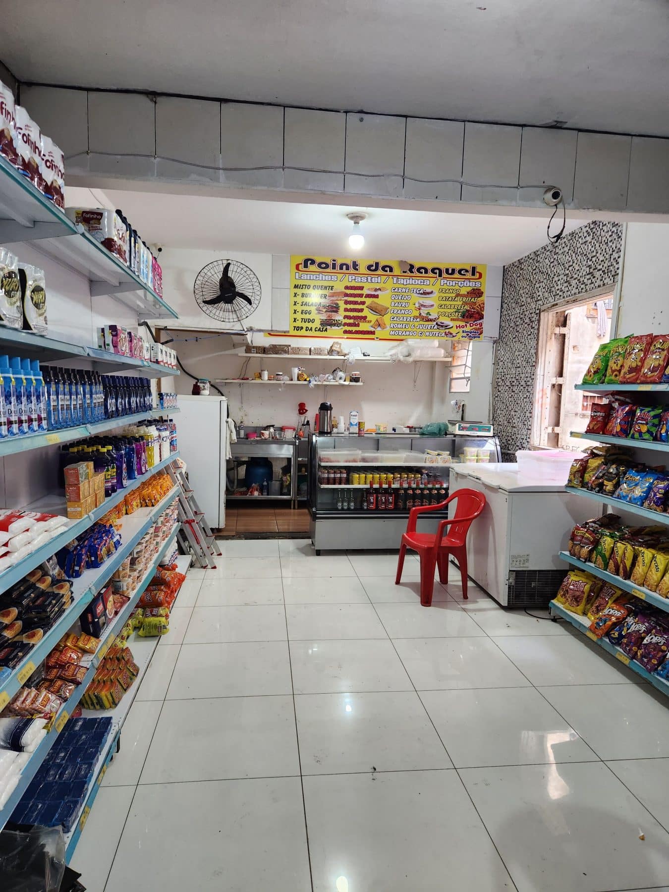 The interior of an empty convenience store. A menu at the front of the shop reads "Point da Raquel"