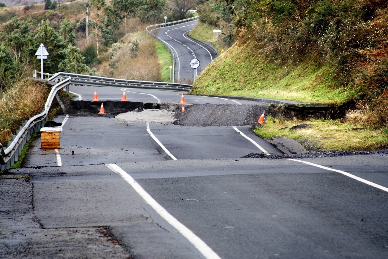 From the middle of a road, the view is of a broken, undriveable road, with gaps and upheavals.