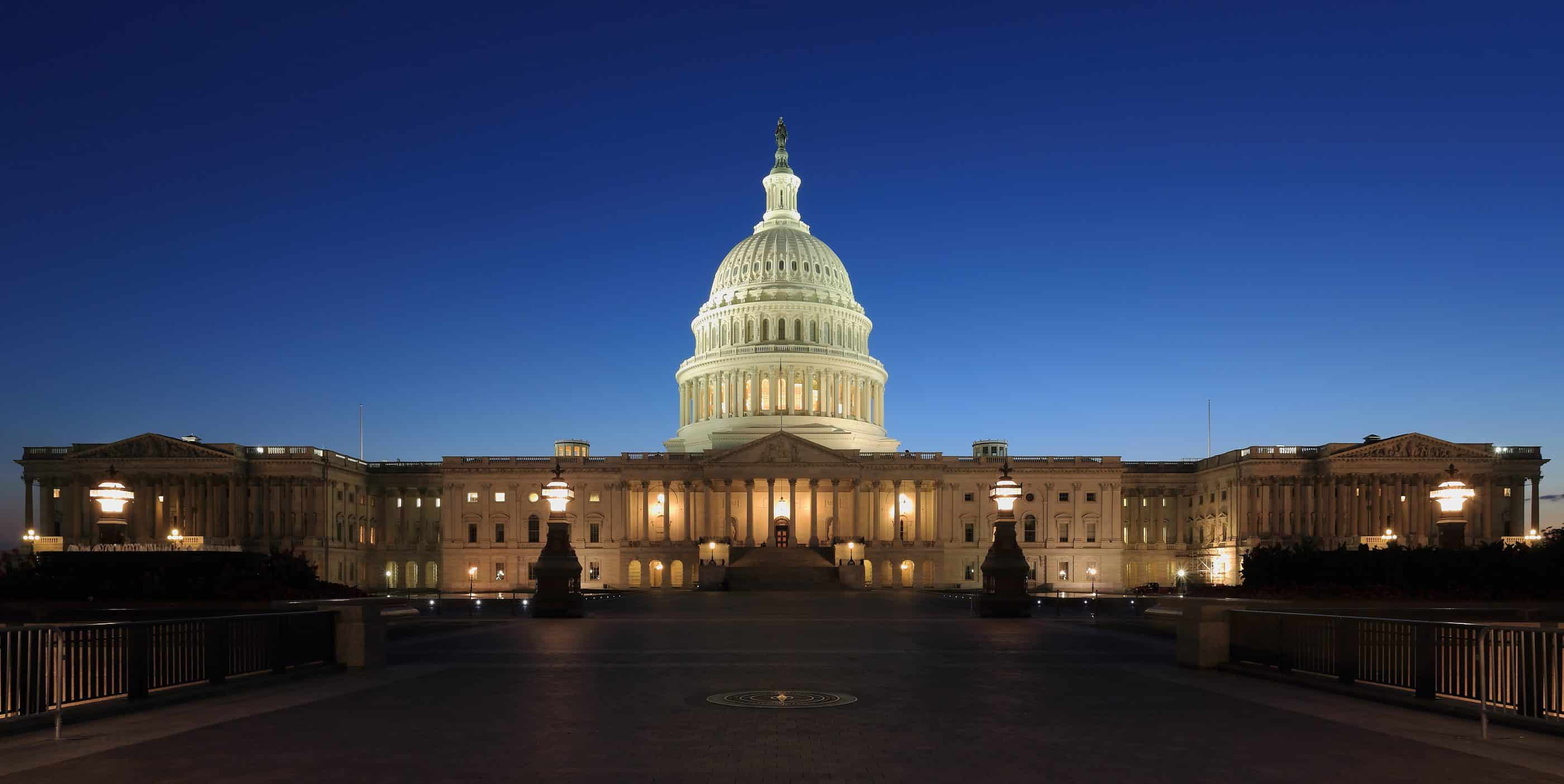 View of the U.S. Capitol at dusk, with a darkening blue sky, bright dome, and warm glowing exterior lights on the building.