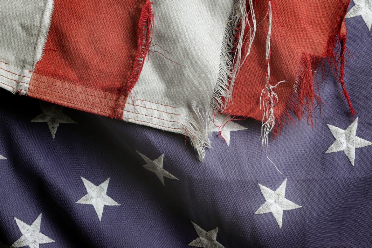 Close view of parts of a tattered flag. The red and white stripes are seriously frayed and can't be resewn. The blue background is faded in places to a light blue.