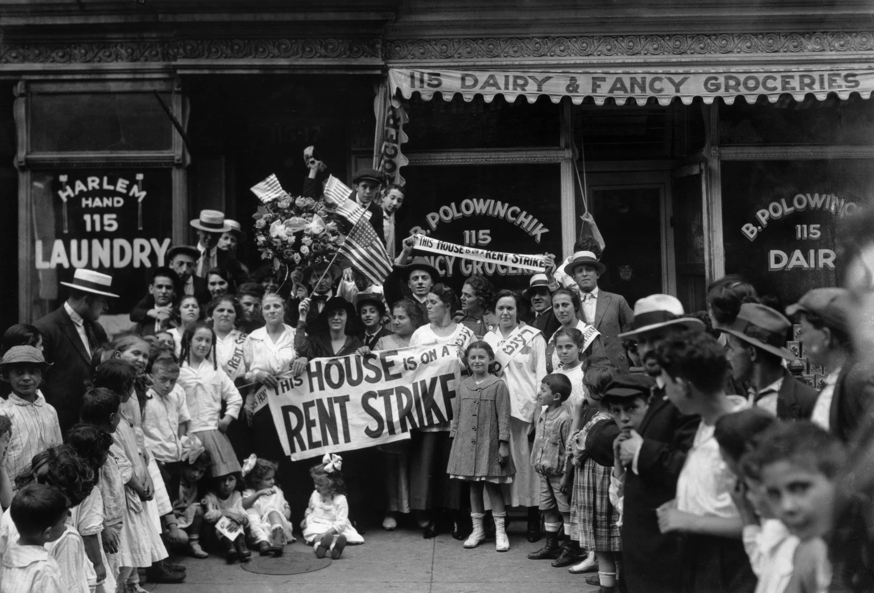 In black and white, a crowd of people hold a sign that says "this house is on a rent strike"