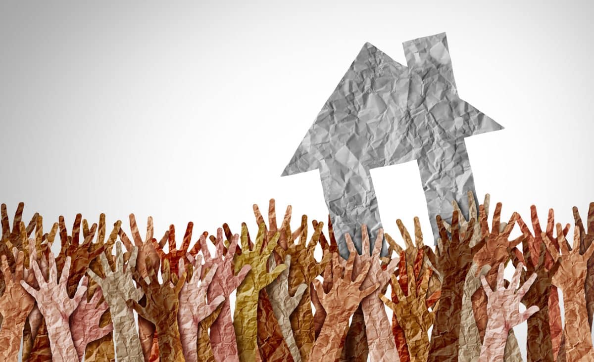 A home in black and white above a group of diverse home buyers reaching for real estate.