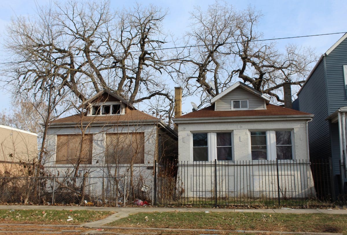 Two bungalow-style homes next to each other, one with its windows boarded up.