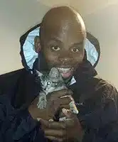 A headshot of a man smiling, holding a kitten.