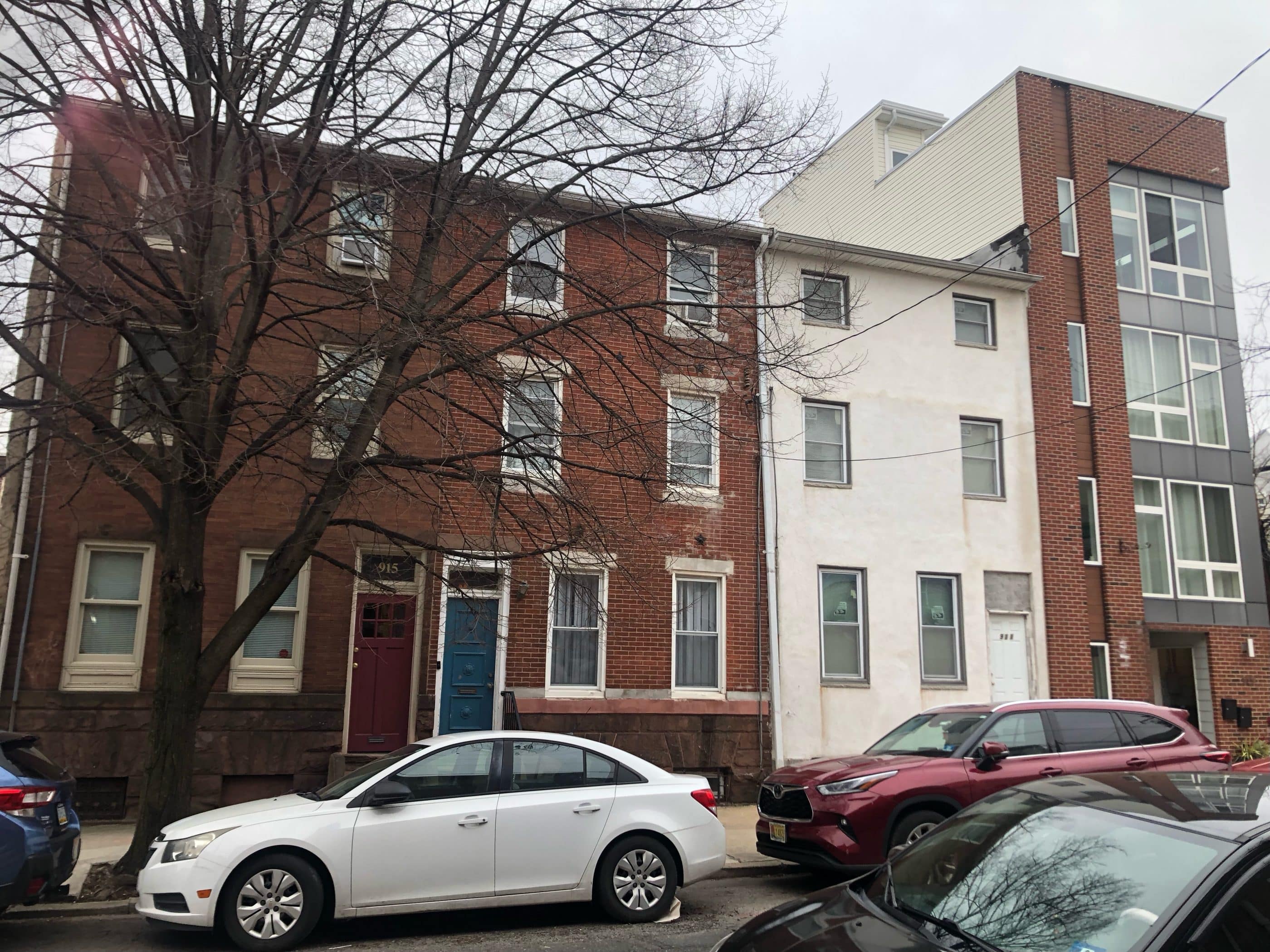 A row of brick and stucco residential row houses in Philadelphia's Francisville neighborhood. The homes overlook a public, one-way street, where cars are parked on either side of the street.
