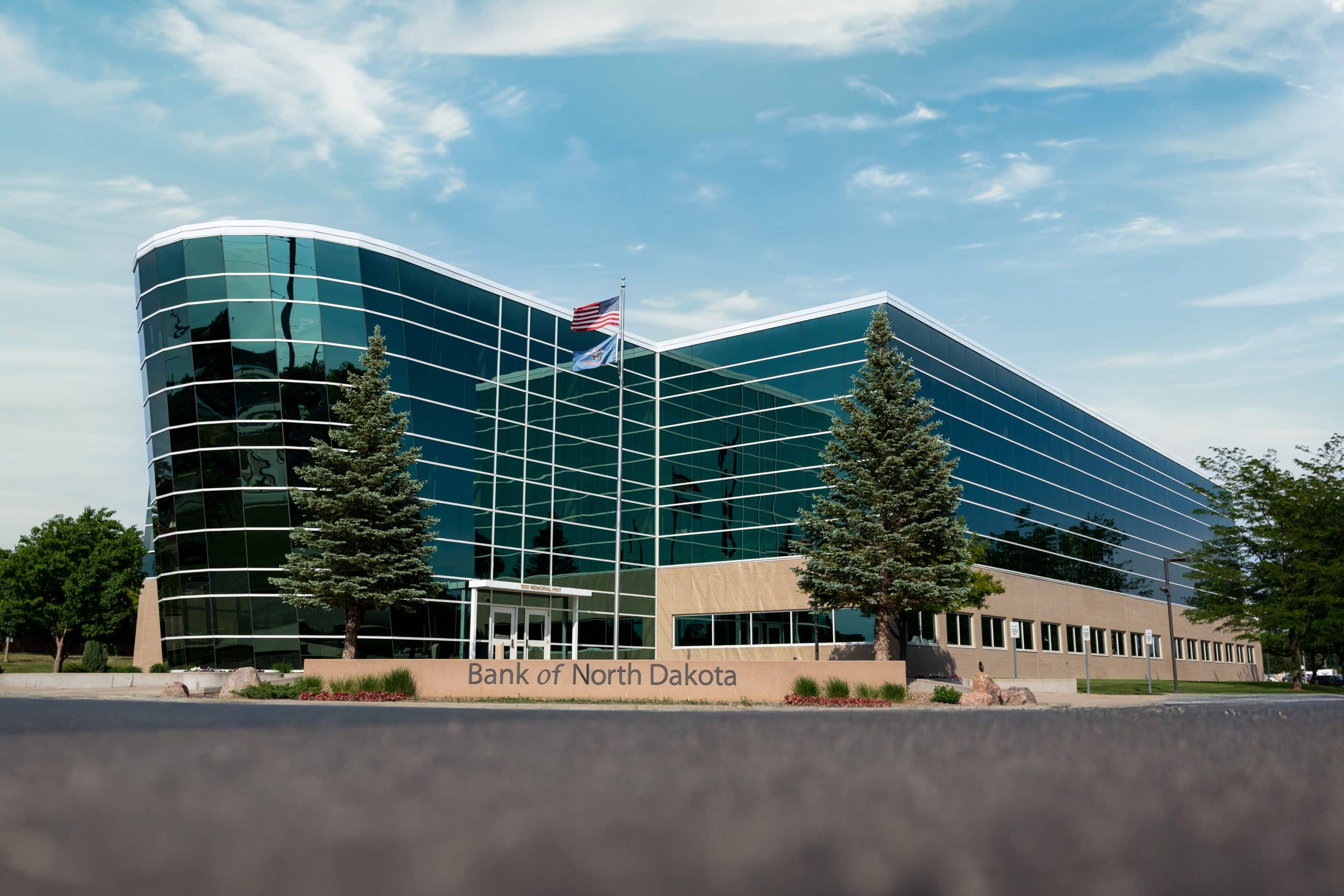 A large glass building set back from a parking lot. In front of the building is a concrete sign coming out of the ground that reads "Bank of North Dakota."