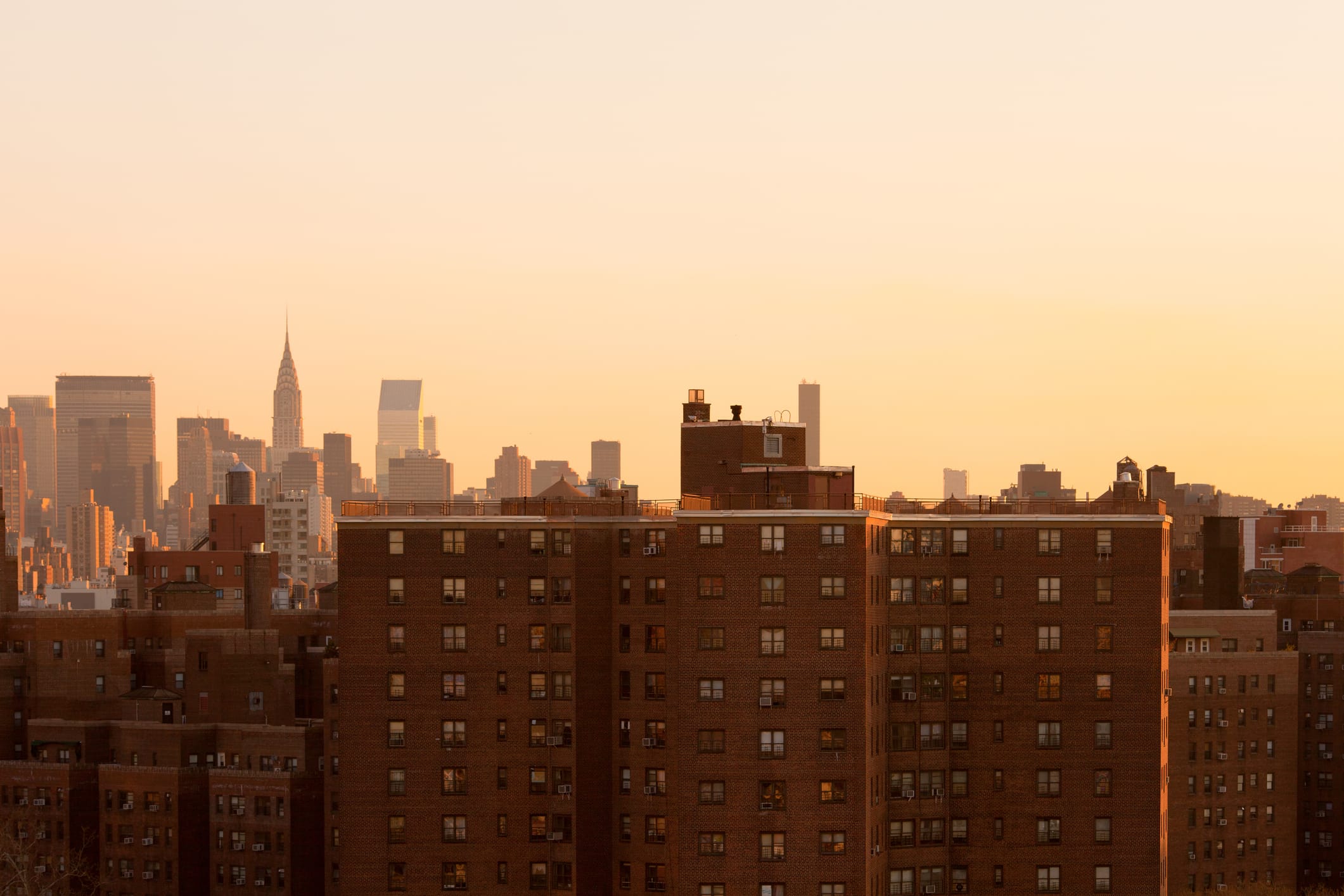 The NYC skyline in golden light, with brick buildings in front.
