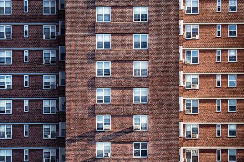 The exterior of a large brick apartment building with many windows. Some of the windows have air-conditioning units.