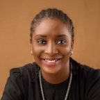 A black woman smiles for the camera. She is wearing a black shirt with a silver chain.