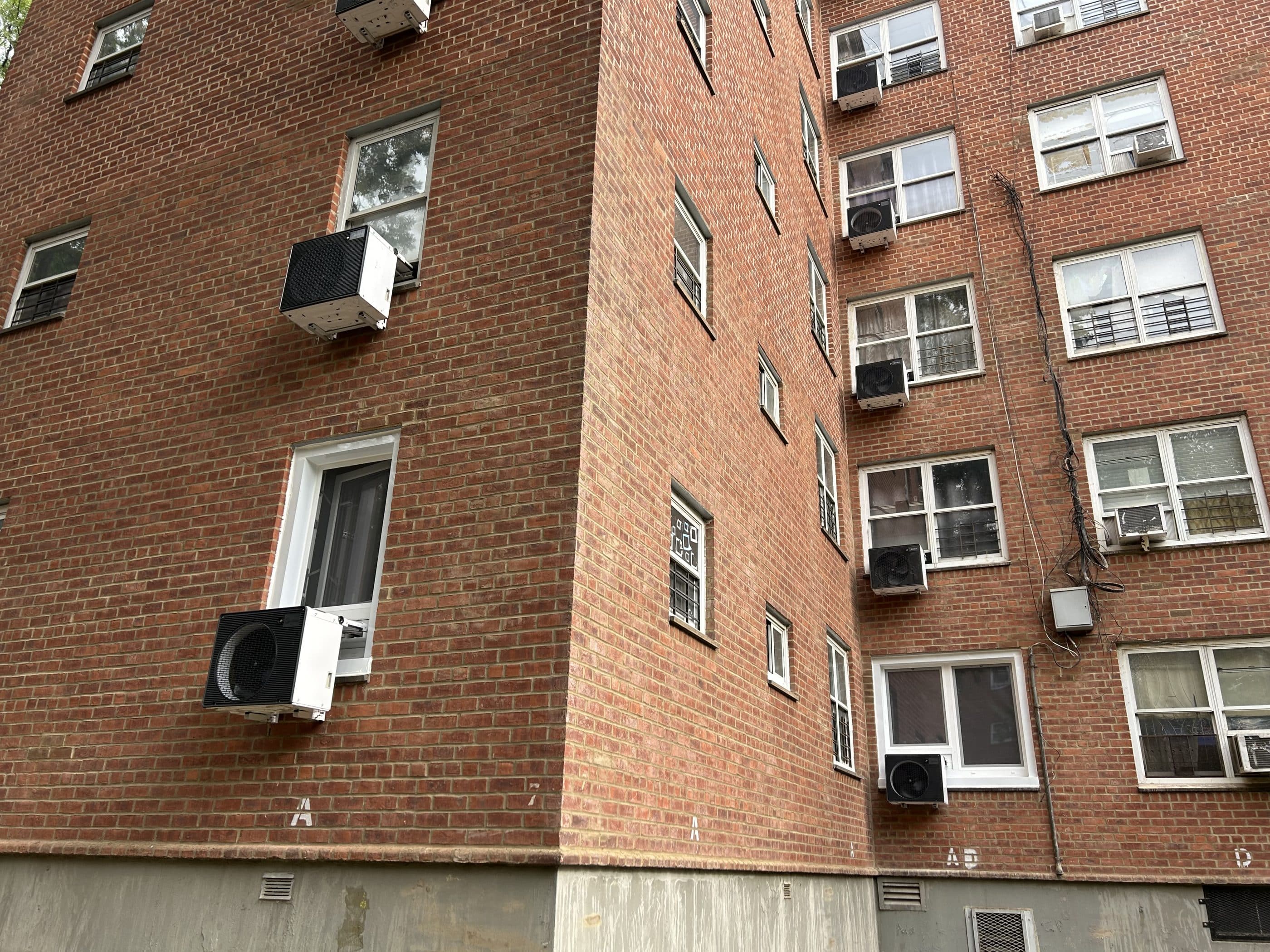 The exterior of a brick apartment building with large heat pumps in the windows.