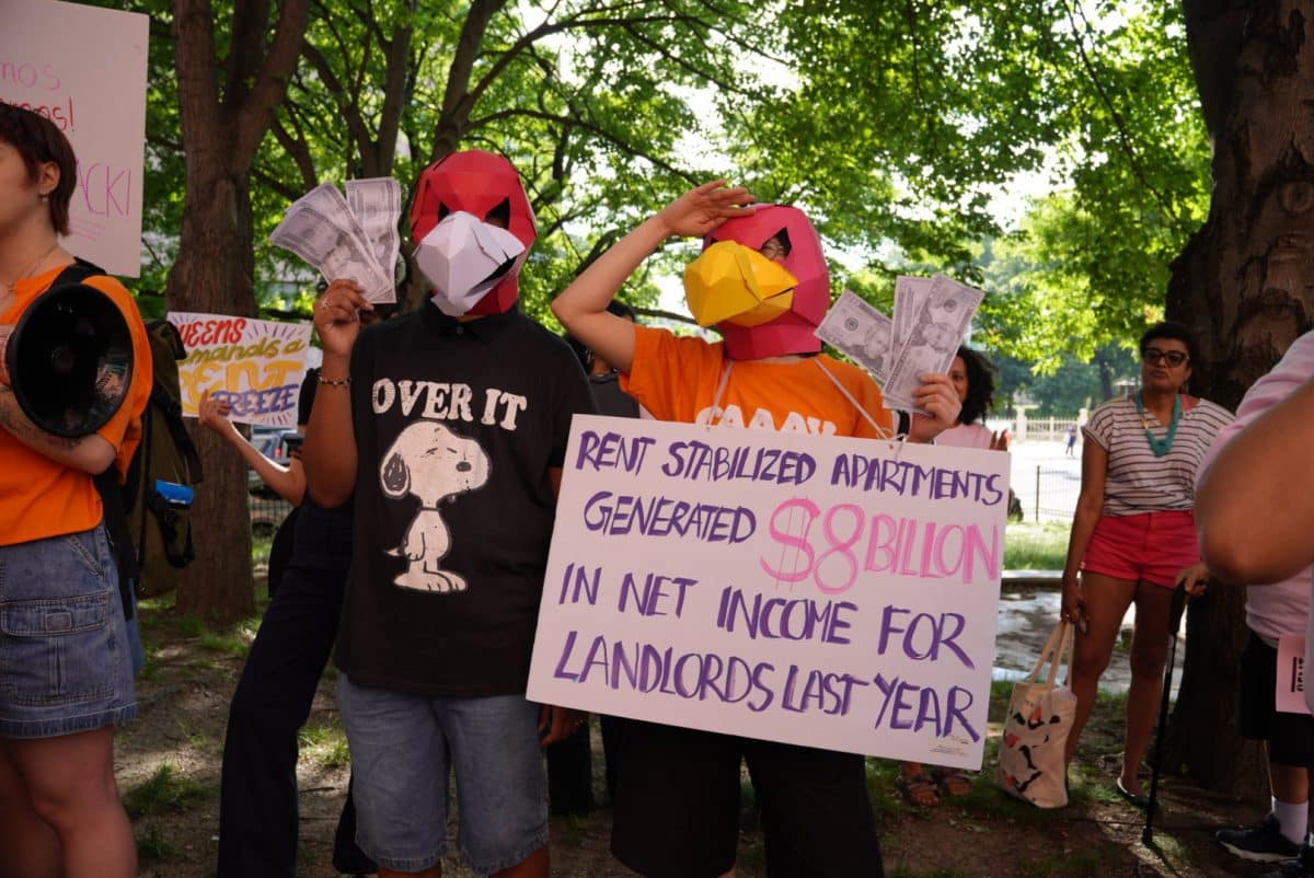 Two people with paper bird masks hold dollar bills. One wears a sign that says "Rent stabilized apartments generated $8 billion in net income for landlords last year."