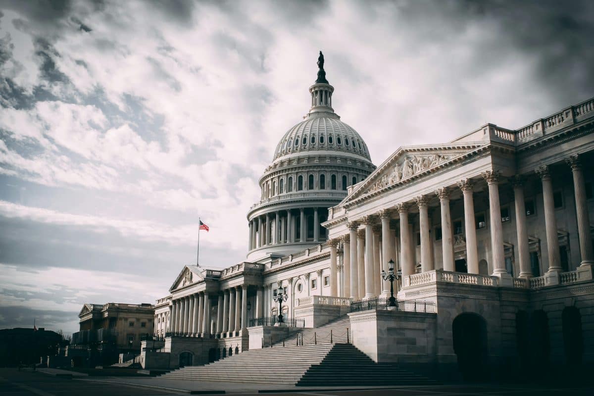 The United States Capitol—a large, white government building—set against a cloudy, stormy-looking sky.
