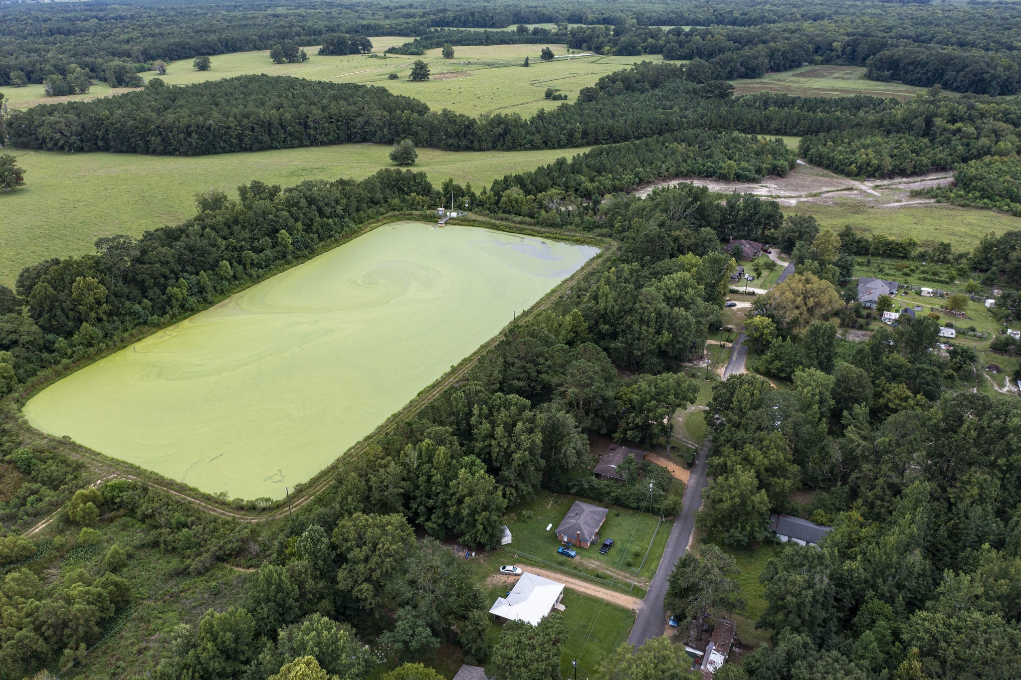 An aerial view of a town with lots of greenery and fields and a large rectangular, green lagoon.