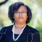 Headshot of Sharlene Newman: a Black woman with curly hair and glasses, wearing formal attire and pearls.